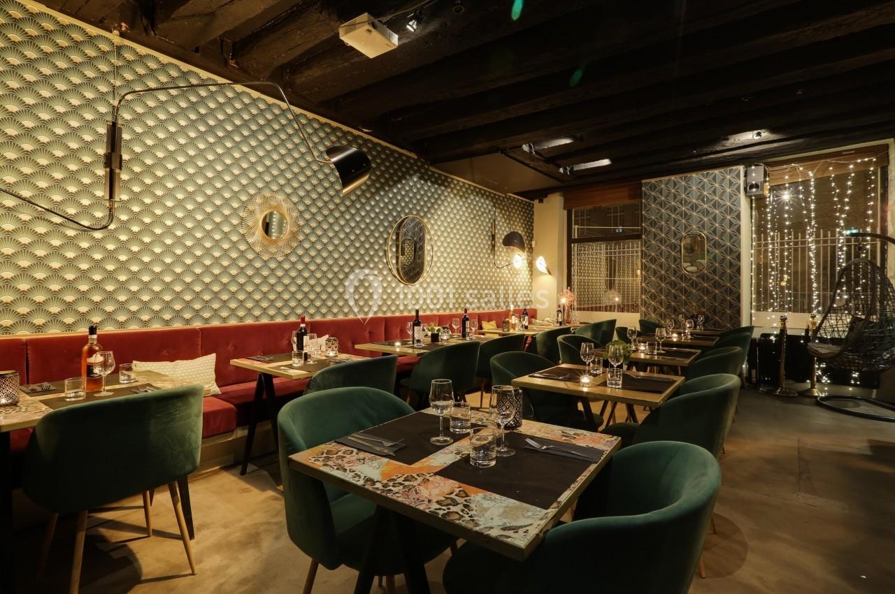 Salle de restaurant avec tables dressées, chaises vertes, banquettes rouges et éclairage tamisé.
