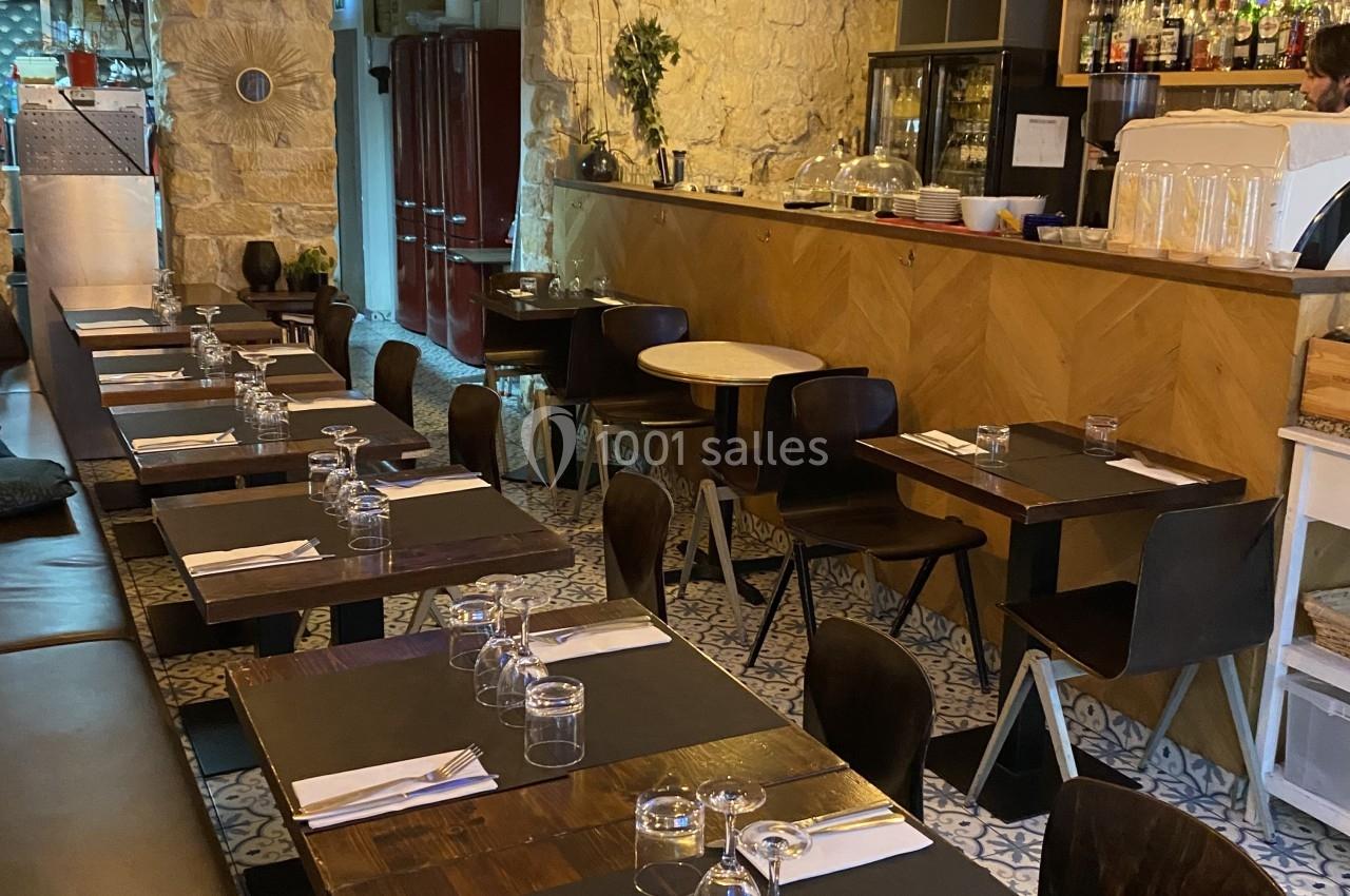 Salle de restaurant avec tables en bois dressées, bar en arrière-plan et éclairage chaleureux.