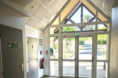 Cuisine professionnelle vide avec plans de travail en inox, murs carrelés blancs, fenêtres et extincteur visible.