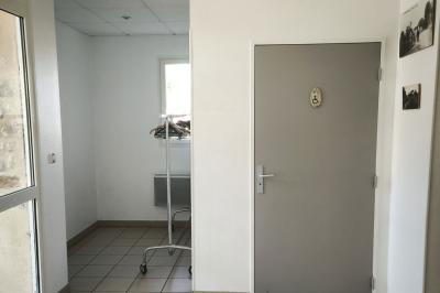 Cuisine professionnelle vide avec plans de travail en inox, murs carrelés blancs, fenêtres et extincteur visible.