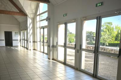 Cuisine professionnelle vide avec plans de travail en inox, murs carrelés blancs, fenêtres et extincteur visible.