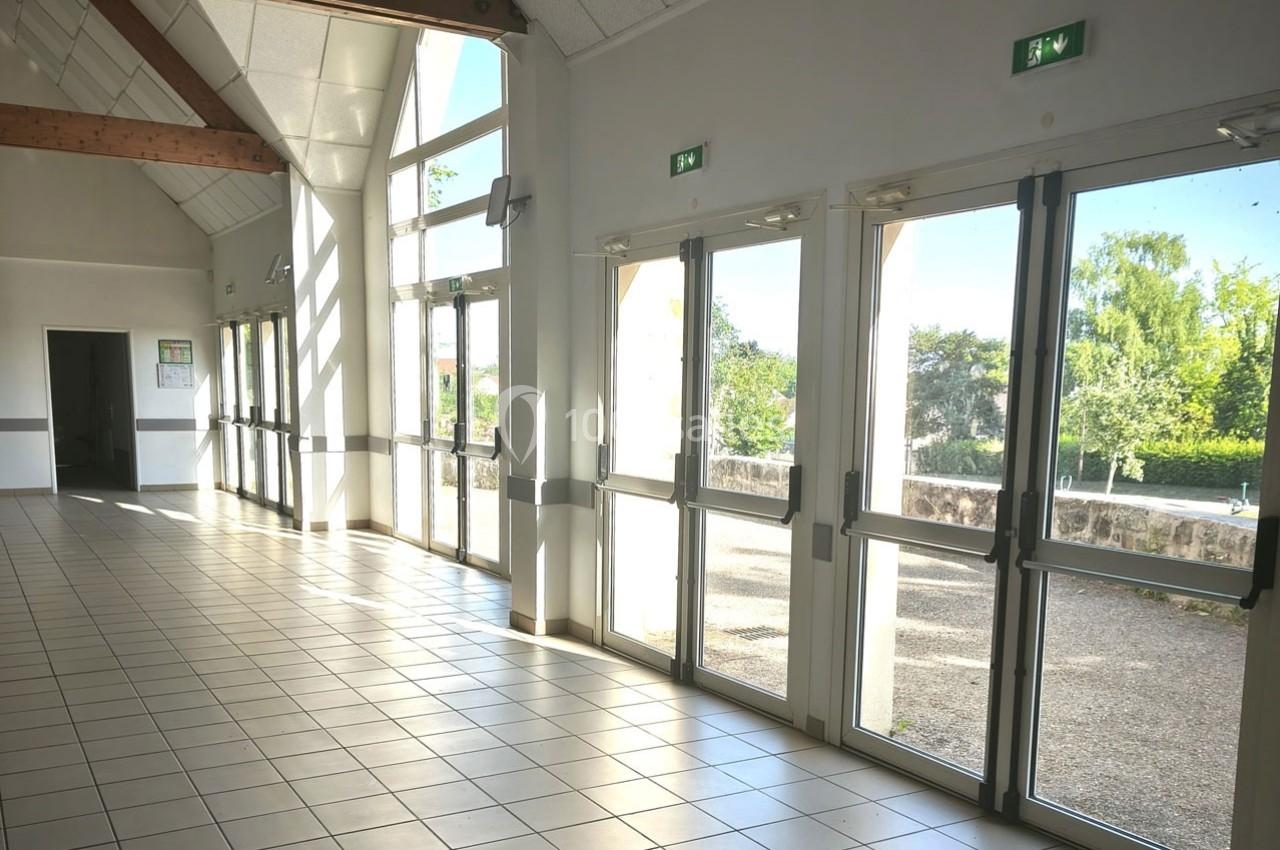 Vue intérieure d'une salle lumineuse avec de grandes baies vitrées donnant sur un espace extérieur arboré.