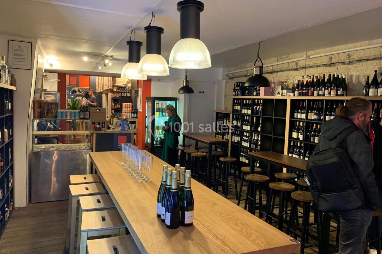Intérieur d'une cave à vin avec des étagères remplies de bouteilles, un comptoir en bois et des tabourets hauts.