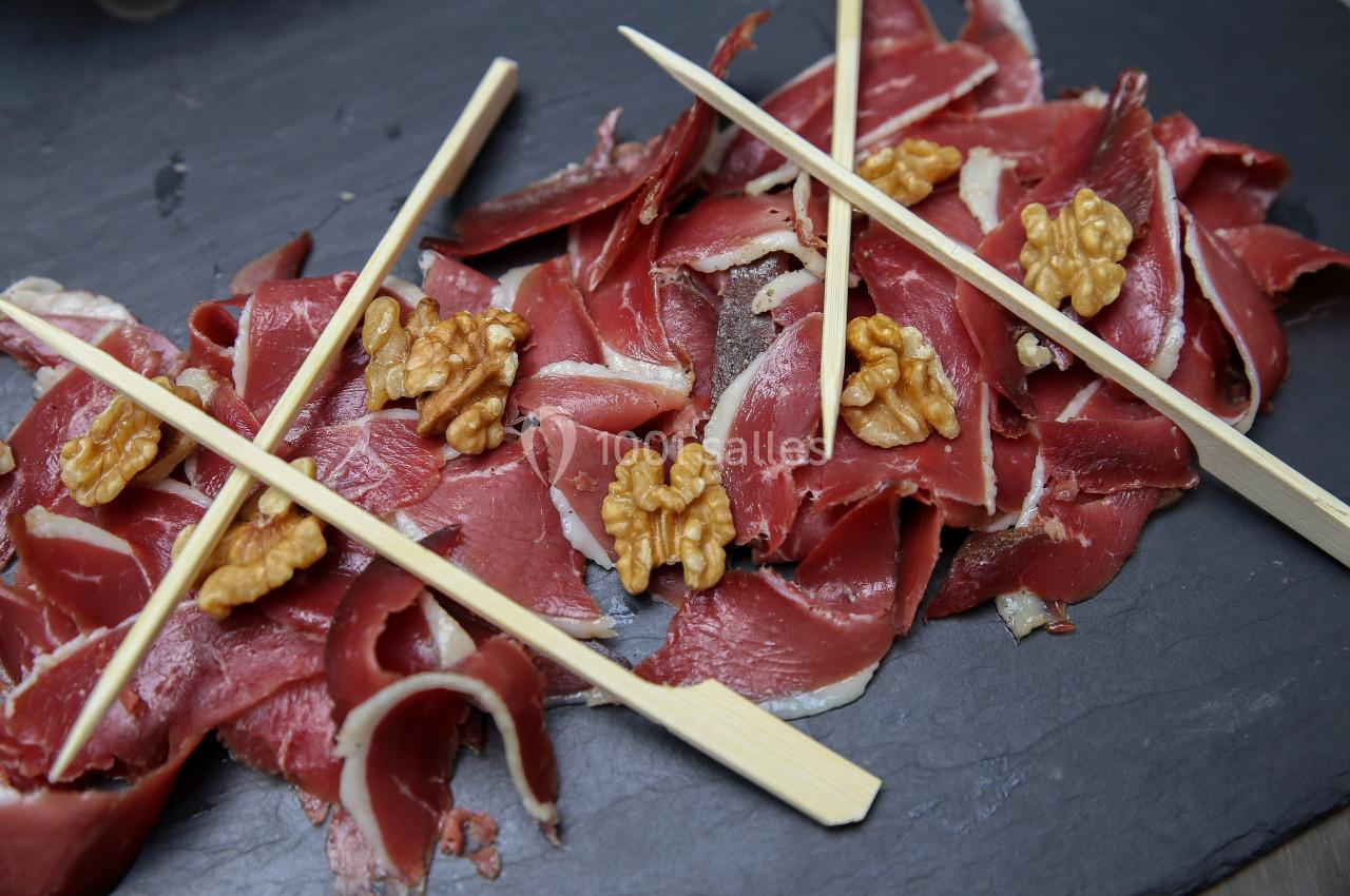 Tranches de viande séchée disposées sur une ardoise avec des noix et des piques en bois.