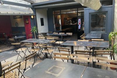 Terrasse extérieure d'un café-restaurant avec tables et chaises en métal et bois, entourée de murs et plantes.