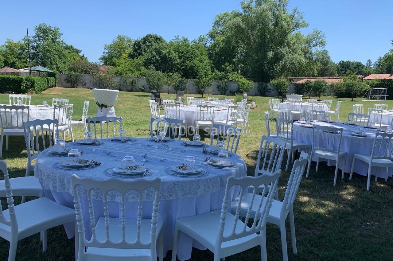 Tables rondes dressées avec nappes blanches et chaises disposées en extérieur sur une pelouse, par une journée ensoleillée.