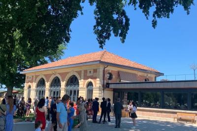 Table ronde élégamment dressée avec des assiettes blanches, des couverts dorés et un bouquet de roses, près d'une baie…