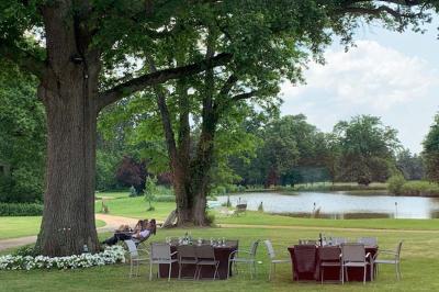 Table ronde élégamment dressée avec des assiettes blanches, des couverts dorés et un bouquet de roses, près d'une baie…