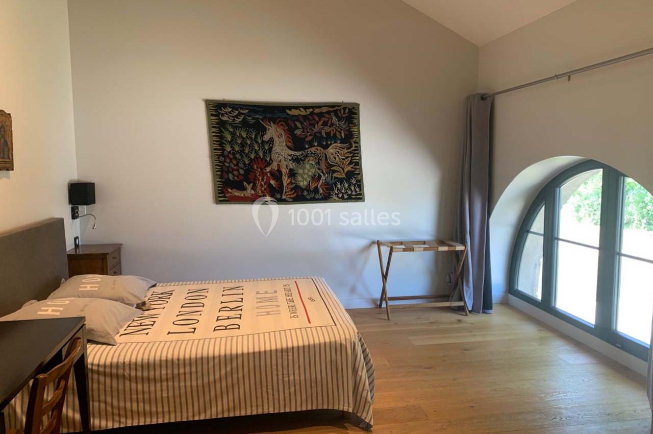 Chambre lumineuse avec un lit double, une tapisserie murale, un bureau en bois et une grande fenêtre cintrée.