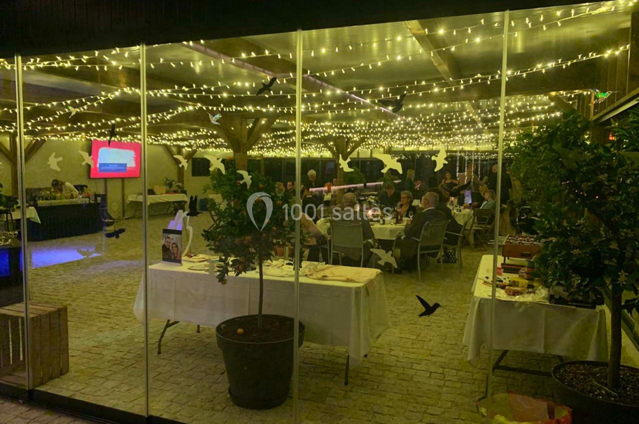 Salle éclairée par des guirlandes lumineuses, avec des tables dressées et des convives assis à l'intérieur.