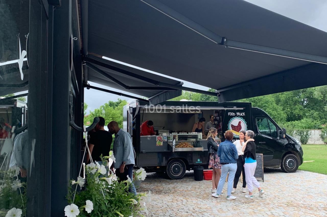Un food truck noir stationné sur une allée pavée, des personnes commandent et discutent à proximité.