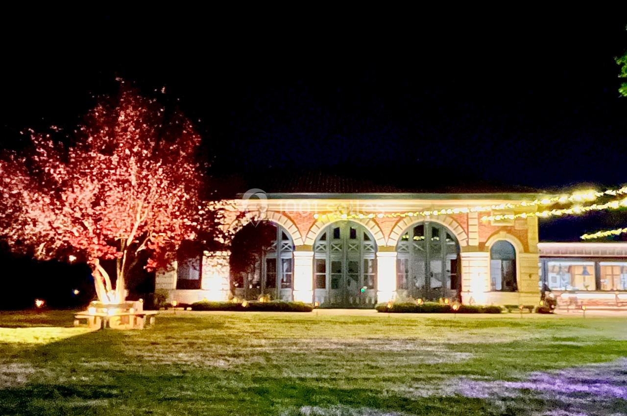 Bâtiment en briques éclairé la nuit, entouré d'arbres illuminés et d'une pelouse.