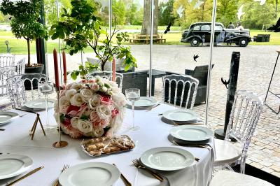 Table ronde élégamment dressée avec des assiettes blanches, des couverts dorés et un bouquet de roses, près d'une baie…