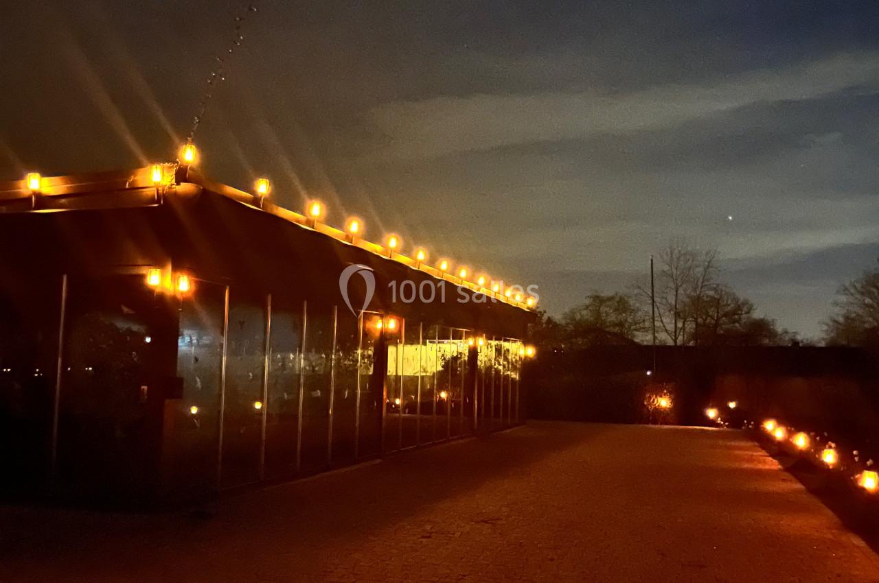 Chemin pavé éclairé par des guirlandes lumineuses et un bâtiment vitré illuminé sous un ciel nocturne.