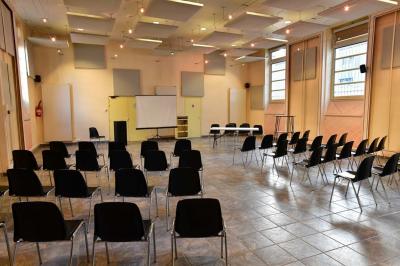 Salle de conférence vide avec des rangées de chaises noires, un écran de projection et des tables à l'avant.