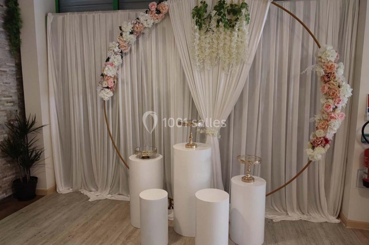 Cercle doré décoré de fleurs, devant un rideau blanc plissé, avec des colonnes blanches et supports transparents.