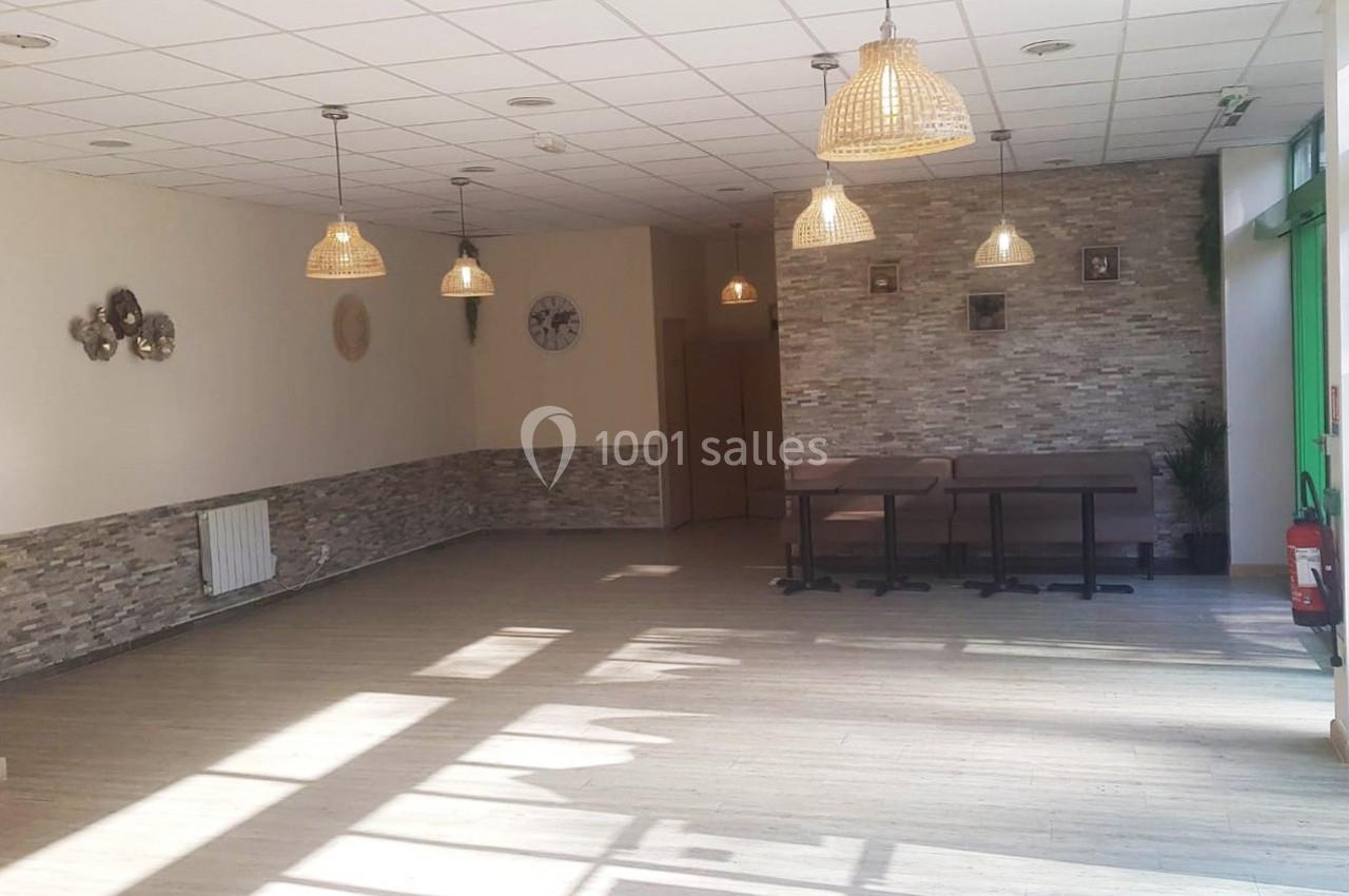 Salle lumineuse avec sol en parquet, murs décorés de pierres et horloges, tables en bois et suspensions en osier.