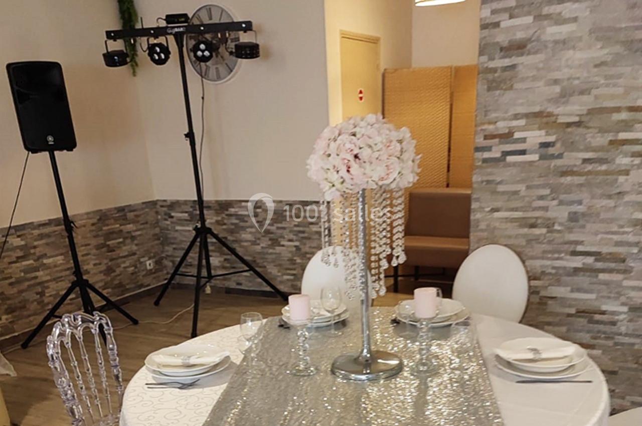 Table décorée avec une nappe argentée, un centre de table floral et des chaises transparentes dans une salle de réception.
