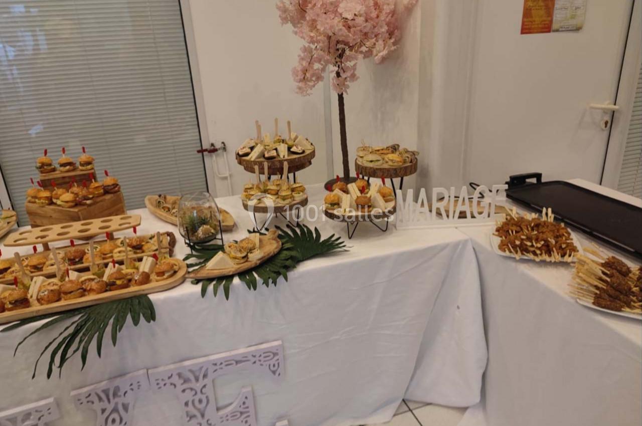 Buffet de réception avec assortiments de bouchées salées, décoré de feuilles tropicales et d'un arbre fleuri rose.