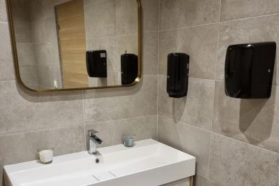 Toilettes modernes avec cuvette suspendue, carrelage gris, mosaïque dorée et accessoires noirs.
