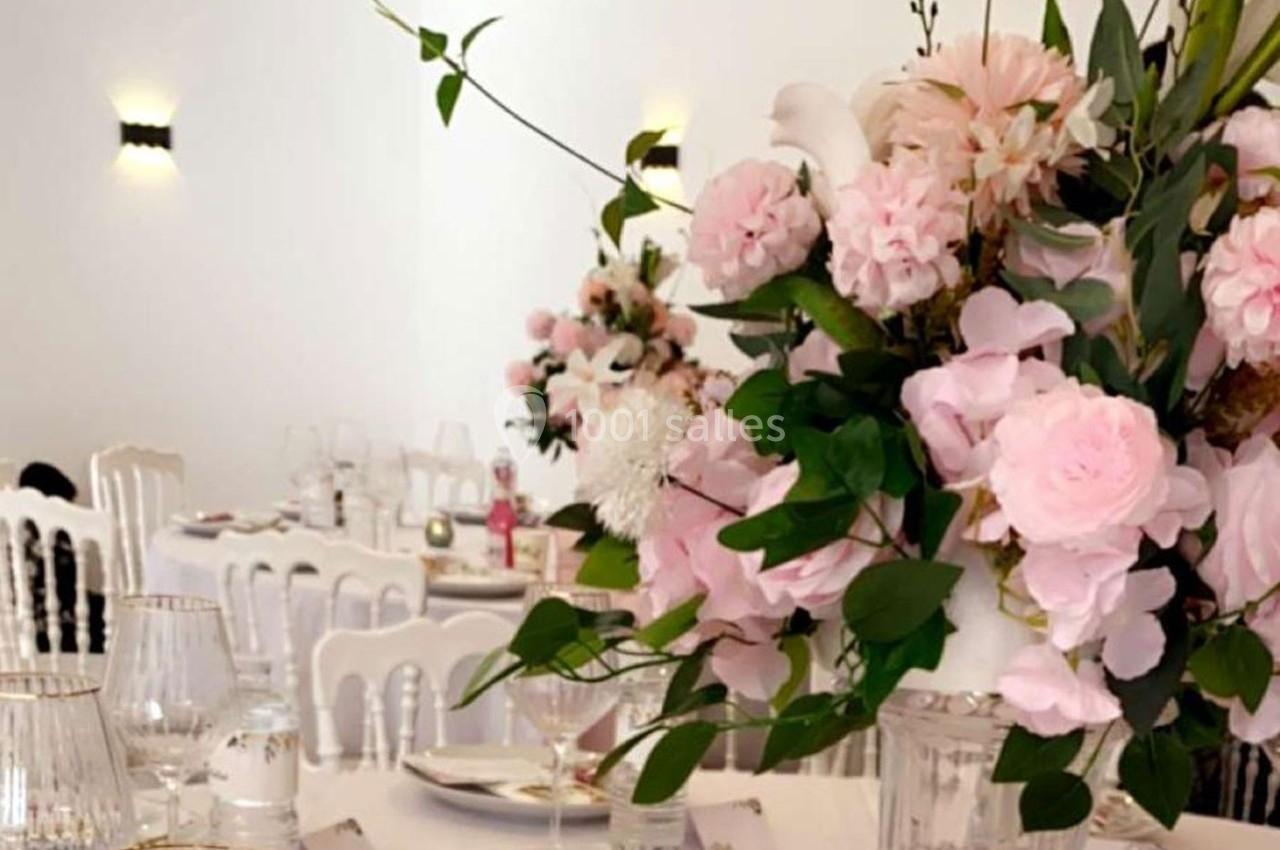 Décoration de table élégante avec des compositions florales roses et blanches, entourées de chaises blanches.