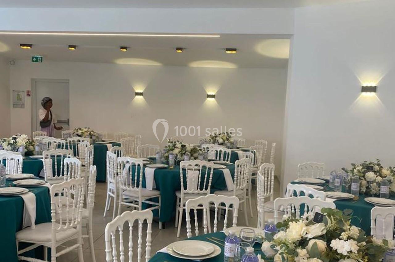 Salle de réception décorée avec des tables dressées, nappes vertes, chaises blanches et arrangements floraux.