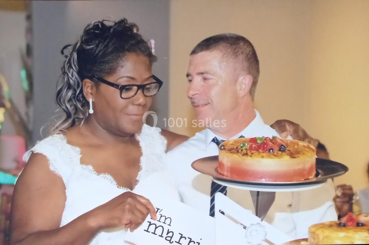 Un couple en tenue de mariage tient un gâteau décoré de fruits dans un cadre festif.