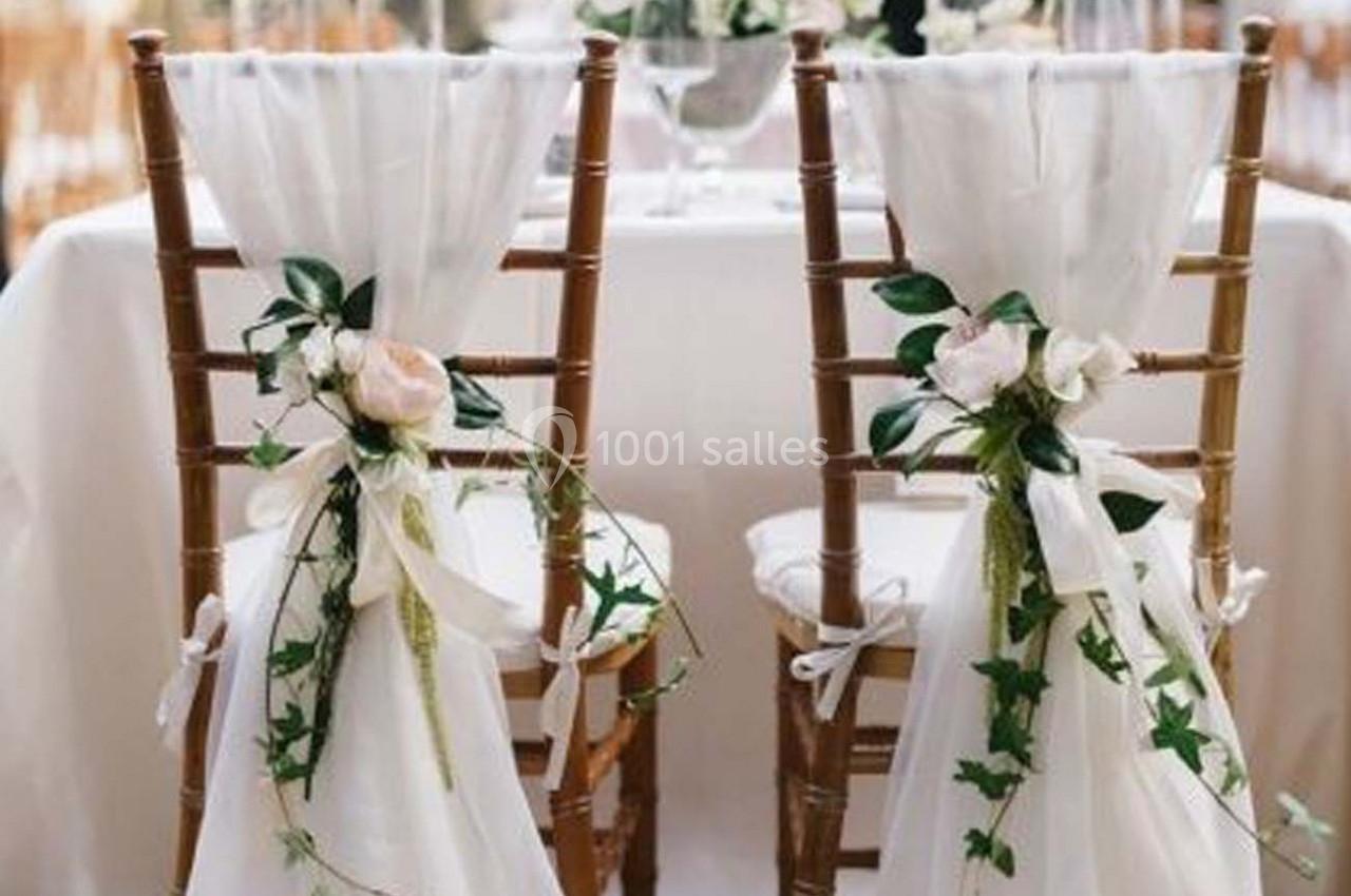 Chaises en bois décorées de tissu blanc et de fleurs, disposées devant une table élégamment dressée.