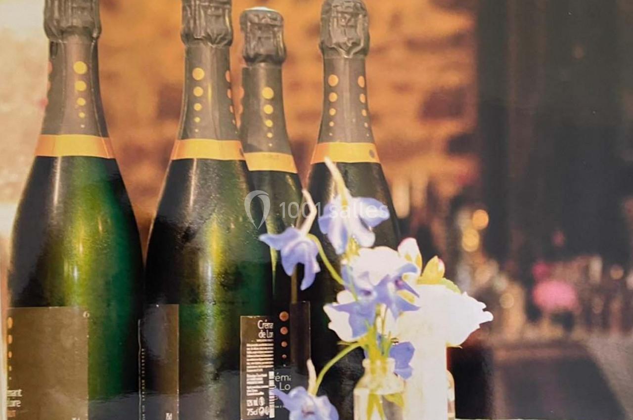 Quatre bouteilles de champagne alignées sur une table avec un vase contenant des fleurs bleues et blanches au premier plan.