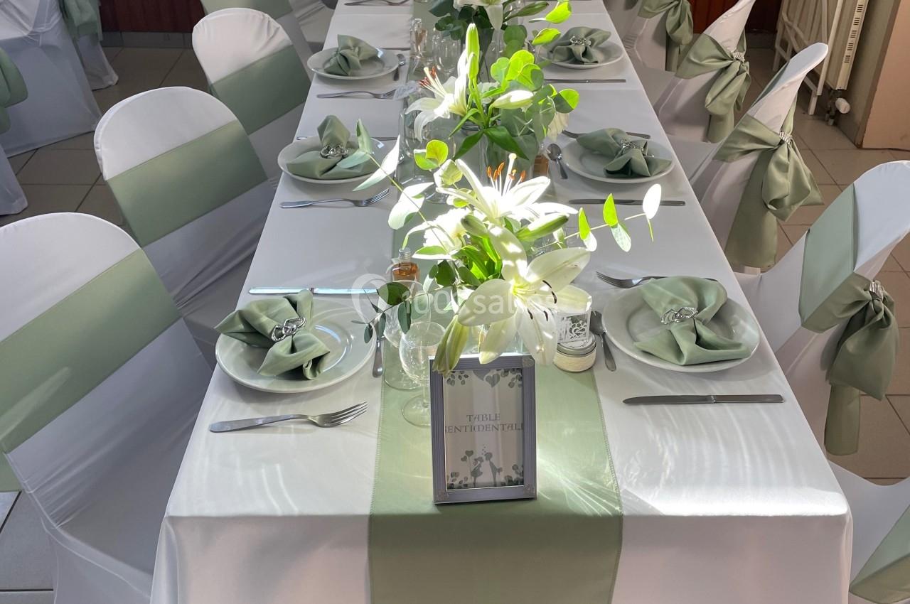 Table décorée pour un événement avec nappes blanches, chemins de table verts, serviettes pliées et arrangements floraux.