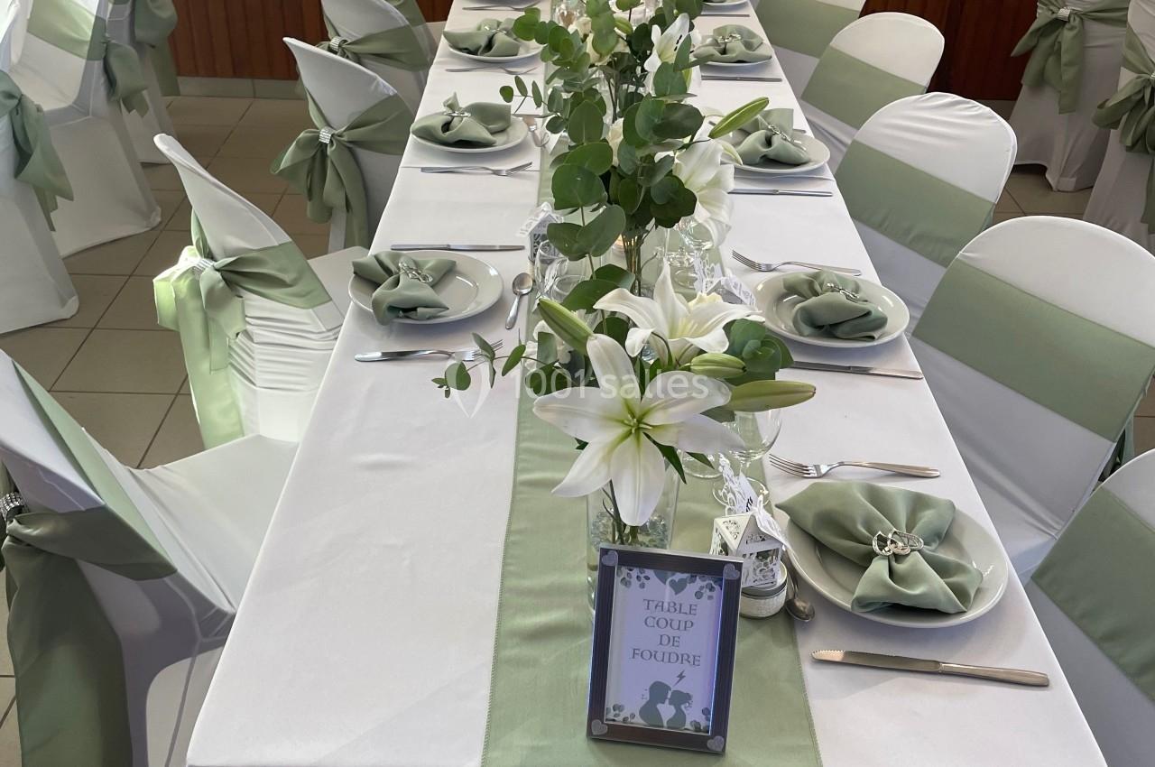 Table décorée pour un événement, nappes blanches, chemins de table verts, serviettes pliées et compositions florales.
