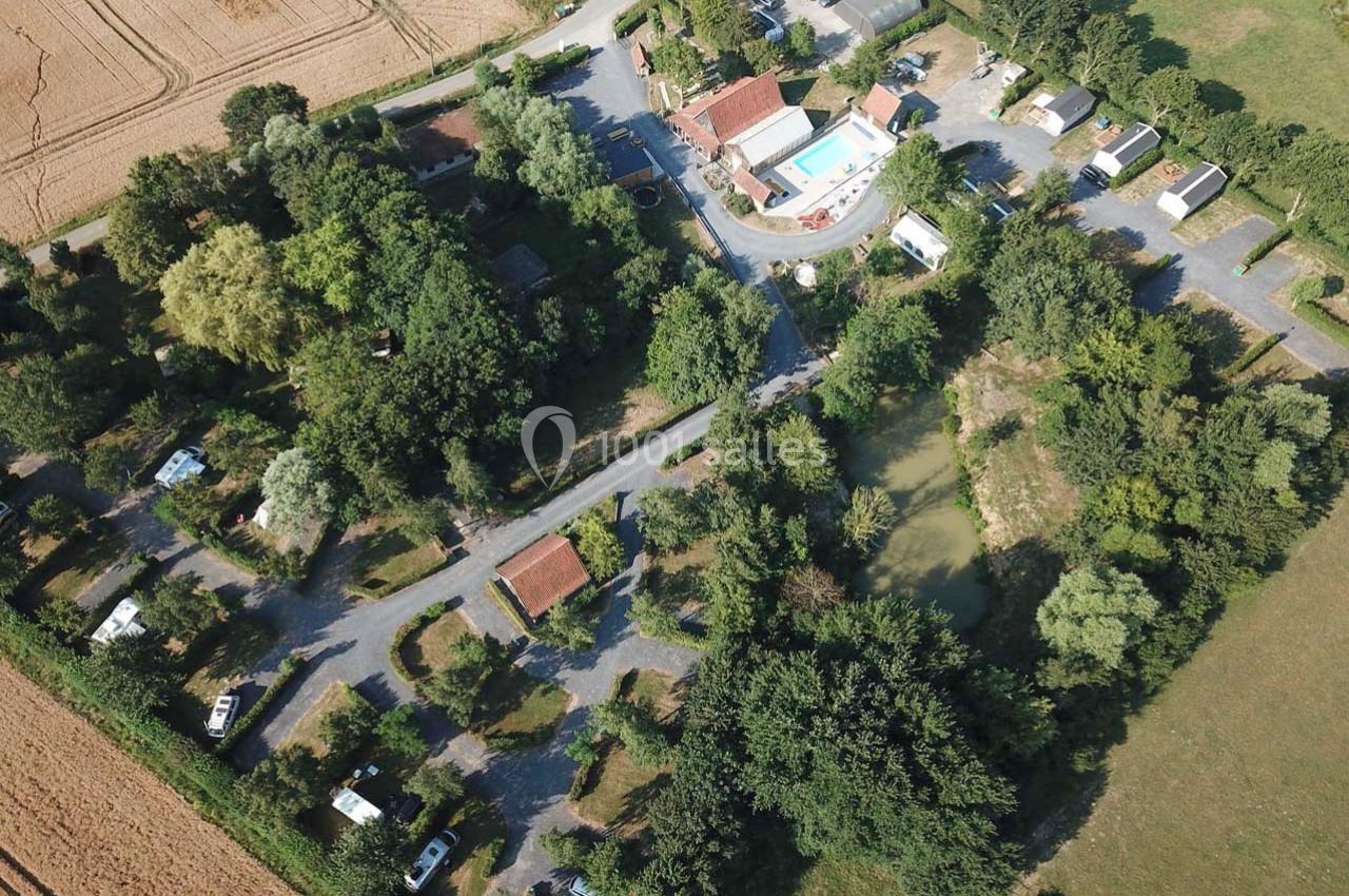Vue aérienne d'un camping avec emplacements, piscine, bâtiments et espaces verts entourés de champs agricoles.