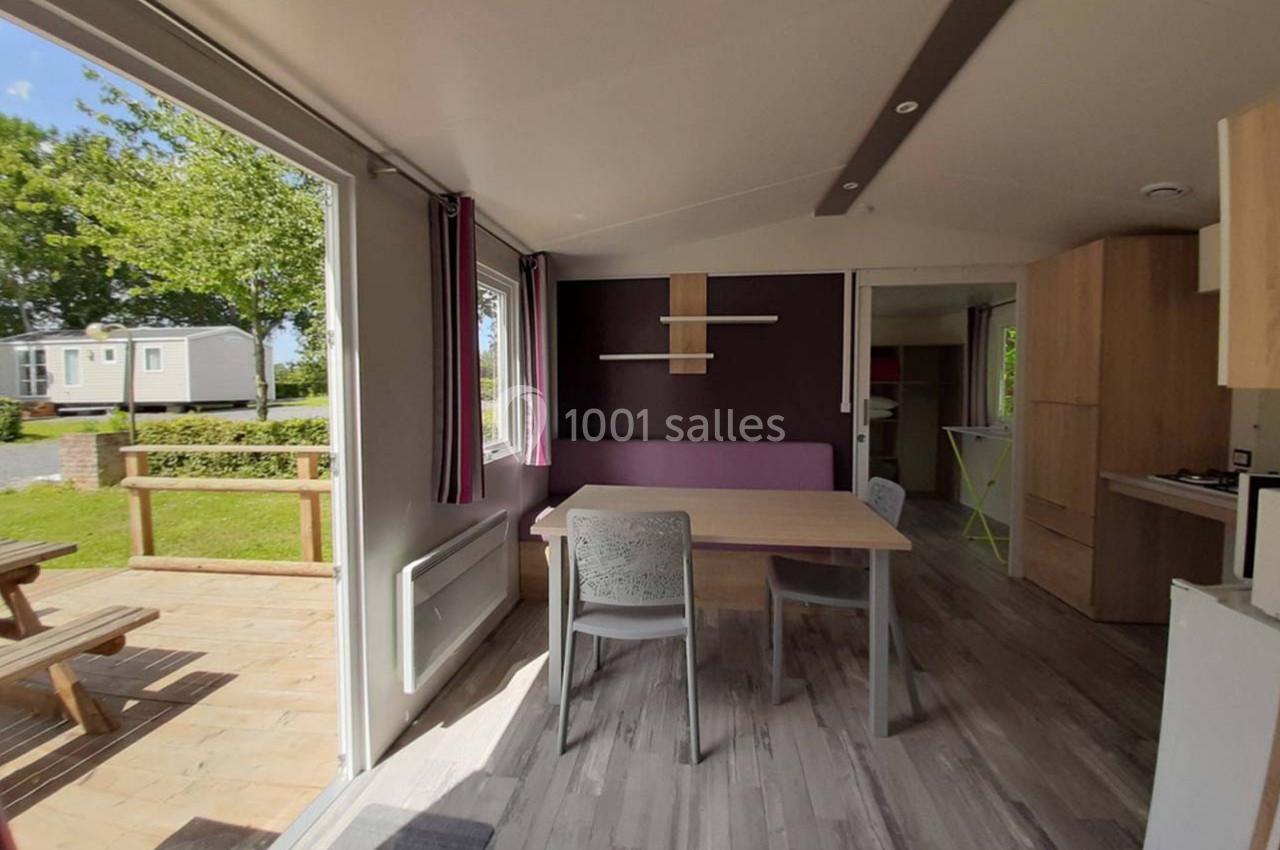 Intérieur lumineux d’un mobil-home avec table, chaises, cuisine équipée et vue sur une terrasse en bois.