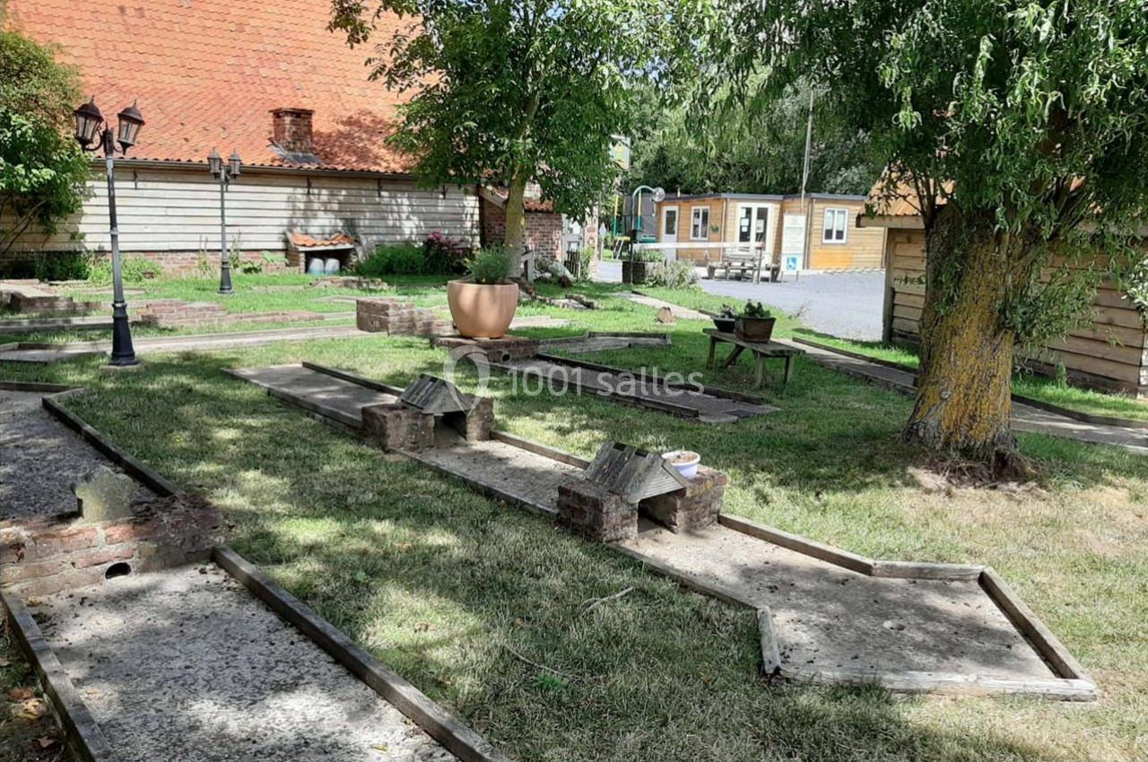 Mini-golf extérieur avec pistes en béton entourées de pelouse, arbres et bâtiments en arrière-plan.