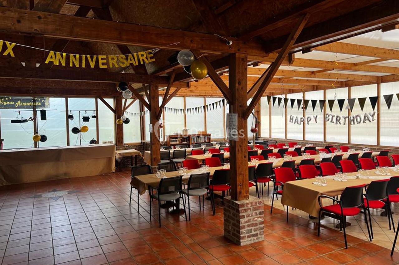Salle décorée pour un anniversaire avec tables alignées, chaises rouges et guirlandes suspendues dans un espace lumineux.