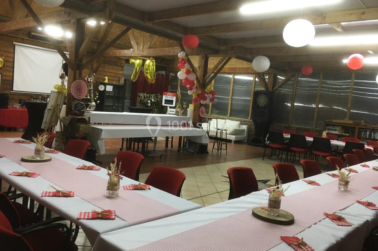Salle décorée pour une réception, avec tables dressées, nappes à carreaux rouges et blanches, et décorations suspendues.