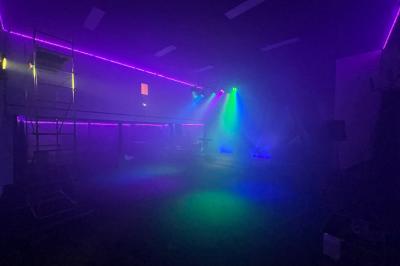 Salle sombre avec éclairage coloré, scène équipée de projecteurs, haut-parleurs et rideaux noirs en arrière-plan.