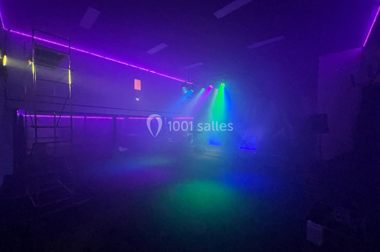 Salle sombre éclairée par des lumières colorées violettes, bleues et vertes, avec une légère ambiance de fumée.