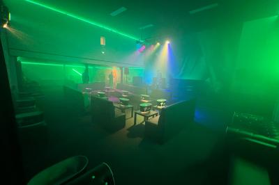 Salle sombre avec éclairage coloré, scène équipée de projecteurs, haut-parleurs et rideaux noirs en arrière-plan.