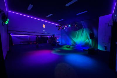 Salle sombre avec éclairage coloré, scène équipée de projecteurs, haut-parleurs et rideaux noirs en arrière-plan.