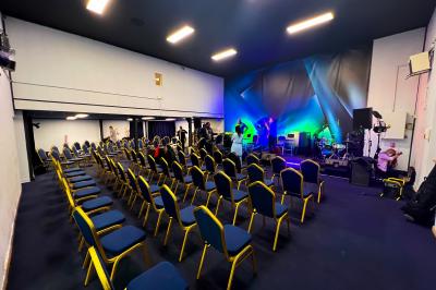 Salle sombre avec éclairage coloré, scène équipée de projecteurs, haut-parleurs et rideaux noirs en arrière-plan.