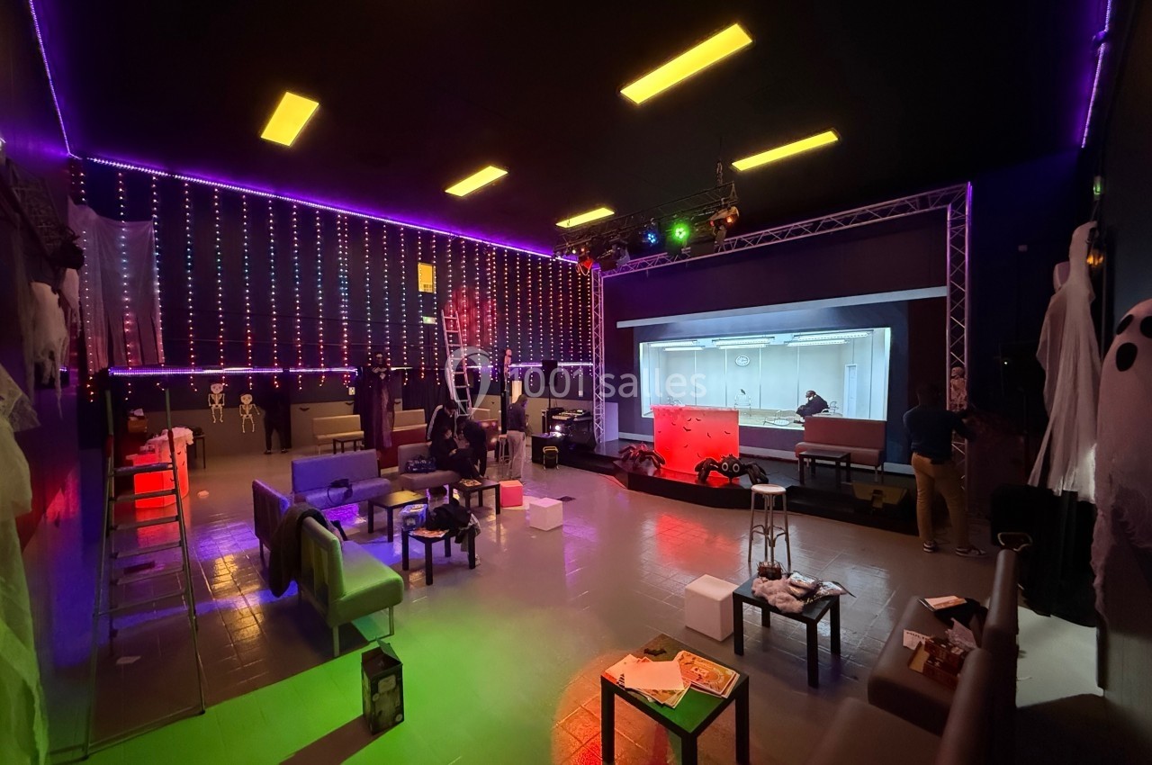 Salle décorée avec des lumières colorées et un grand écran, des meubles dispersés et des personnes en préparation.