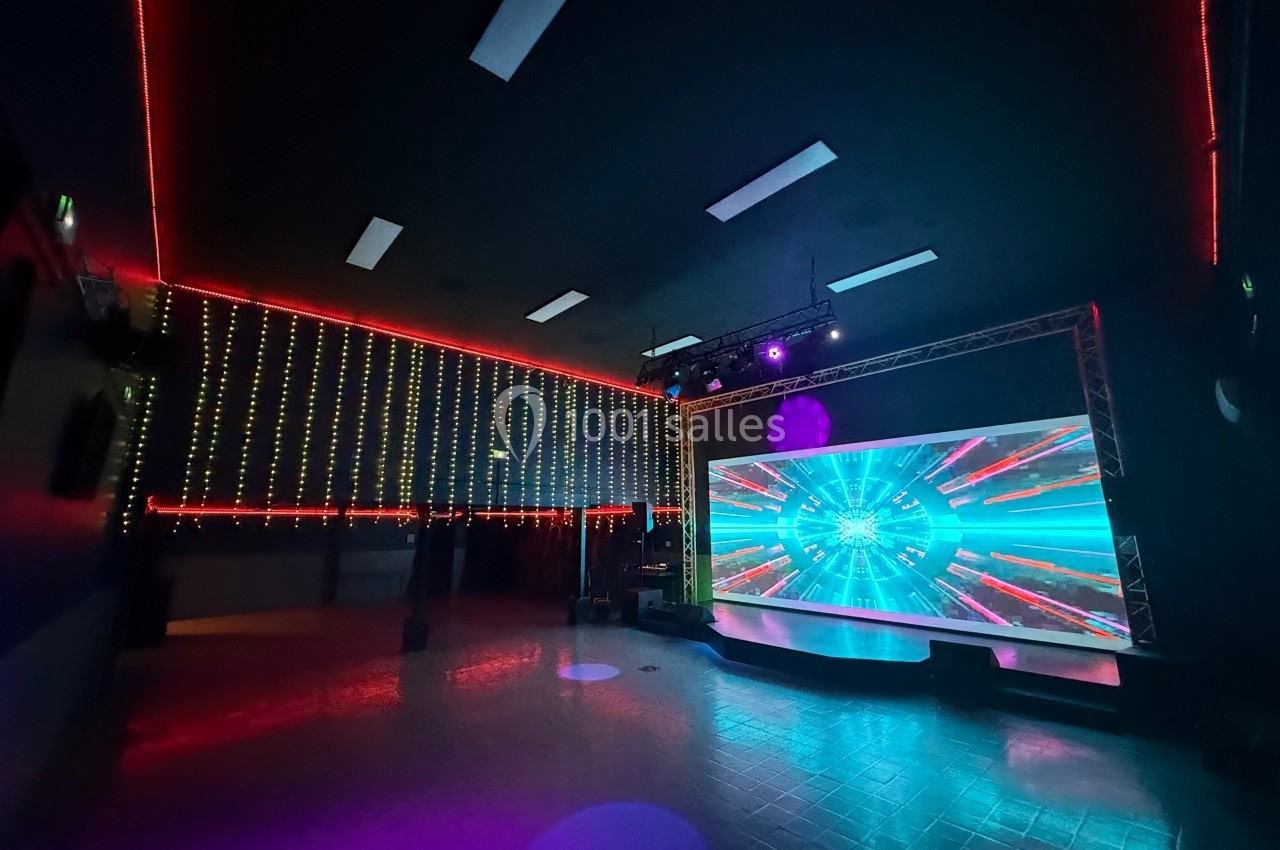 Salle sombre avec écran géant affichant des effets lumineux colorés et murs décorés de guirlandes LED.