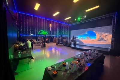Salle de réception décorée avec des tables rondes, nappes bleues, chaises dorées et centres de table floraux blancs.