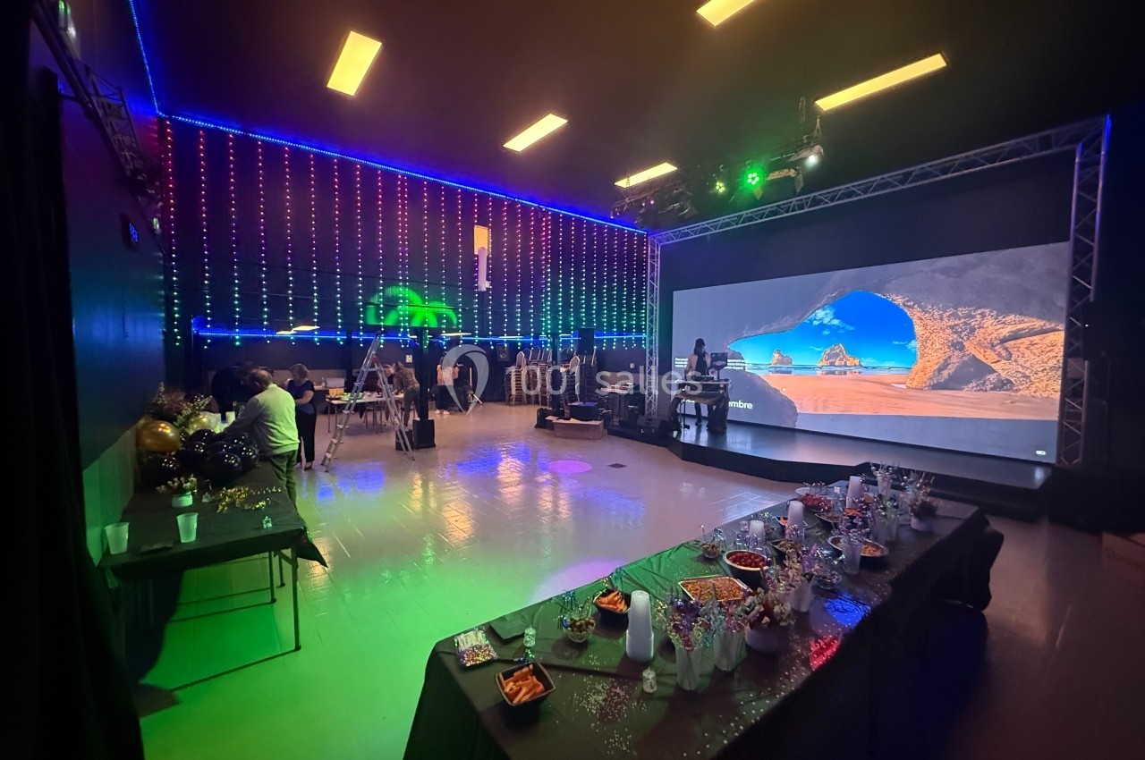 Salle décorée avec des lumières colorées, tables dressées avec des collations et grand écran affichant un paysage.