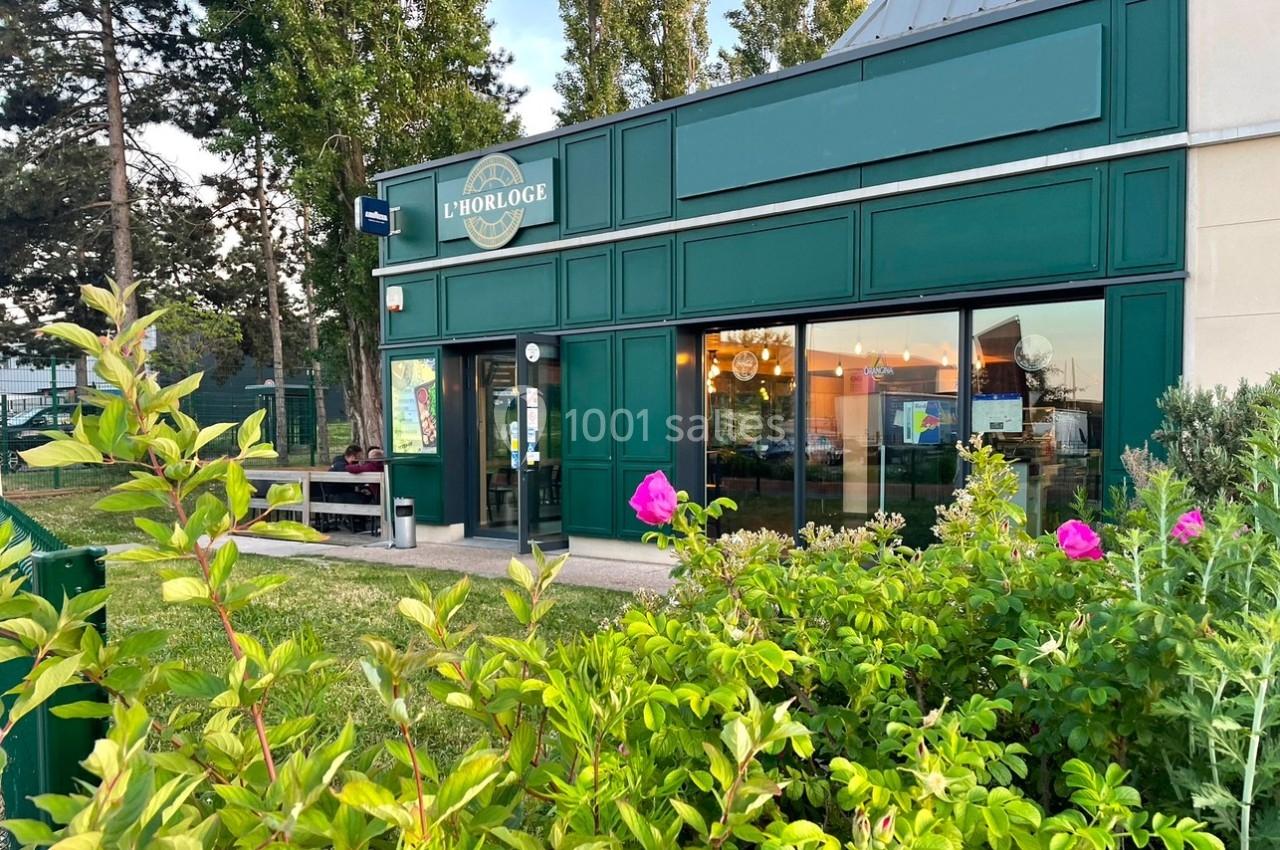 Façade d'un restaurant avec enseigne verte, entouré de végétation et éclairé par la lumière du jour.