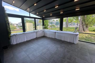 Salle de réception moderne avec tables dressées, sol en carrelage gris, éclairage suspendu et décor floral.