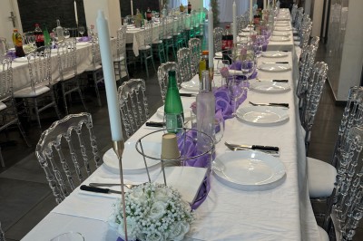 Salle de réception moderne avec tables dressées, sol en carrelage gris, éclairage suspendu et décor floral.