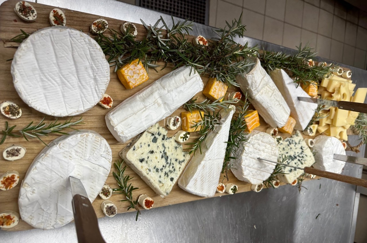 Plateau en bois garni de fromages variés, herbes fraîches et petites garnitures, présenté sur une table en cuisine.