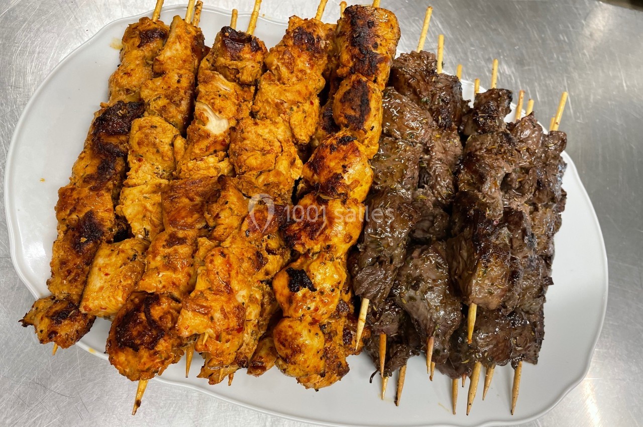 Assortiment de brochettes de poulet mariné et de viande grillée, disposées sur une assiette blanche.